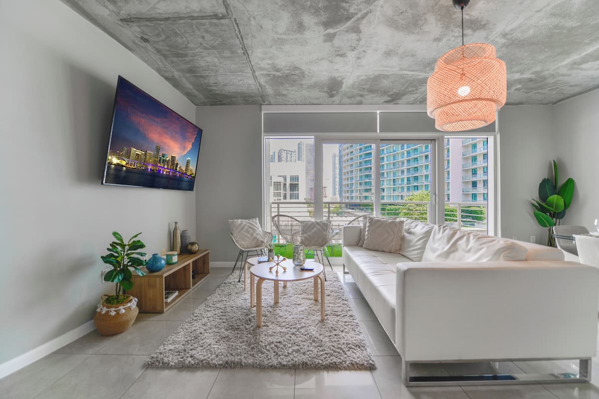 A modern living room with a white sofa, a round coffee table, and a large window offering a city view.