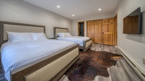 Een slaapkamer met twee bedden, een houten garderobe en een wandtelevisie.