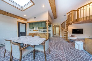 Un vaste espace de vie comprenant un coin repas avec table et chaises, une cuisine équipée d’appareils électroménagers modernes et un escalier en bois menant à l’étage supérieur.
