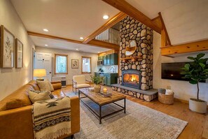 A cozy living room with a fireplace, a sofa, a coffee table, and a TV. - Two-Level Suite with En-Suite Jacuzzi and Steam Shower in Windham (Windham)