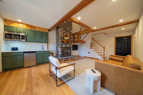 A modern kitchen with green cabinets, a stone fireplace, and a dining area with a sofa and a small table.