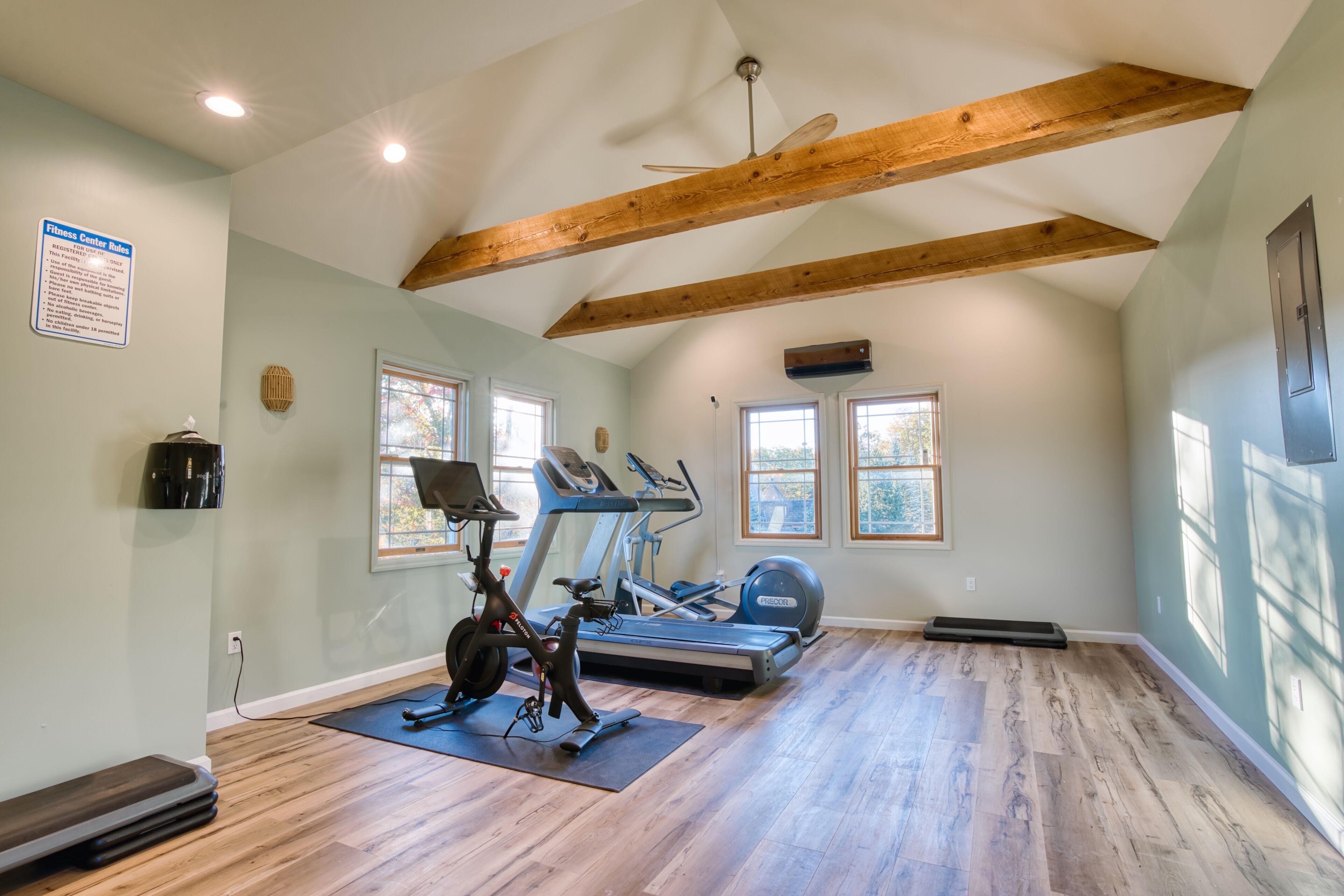 A spacious room with a ceiling fan, wooden beams, a treadmill, an elliptical, and a stationary bike.
