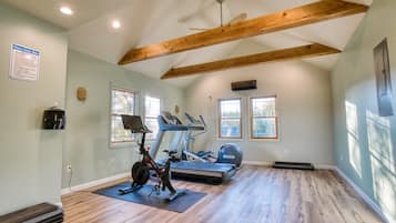 A spacious room with a ceiling fan, wooden beams, a treadmill, an elliptical, and a stationary bike.