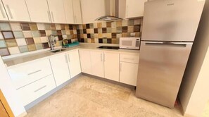 Compact kitchen with modern design, featuring a refrigerator, microwave, and sink with a contemporary faucet.