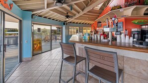A bar area with a counter, bar stools, and a ceiling fan. - 2 BR Updated Admirals Row at HH Beach and Tennis Bikes & Beach Gear included (Hilton Head Island)