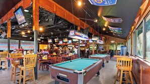 A pool hall with multiple pool tables, wooden chairs, and overhead signs. - 2 BR Updated Admirals Row at HH Beach and Tennis Bikes & Beach Gear included (Hilton Head Island)