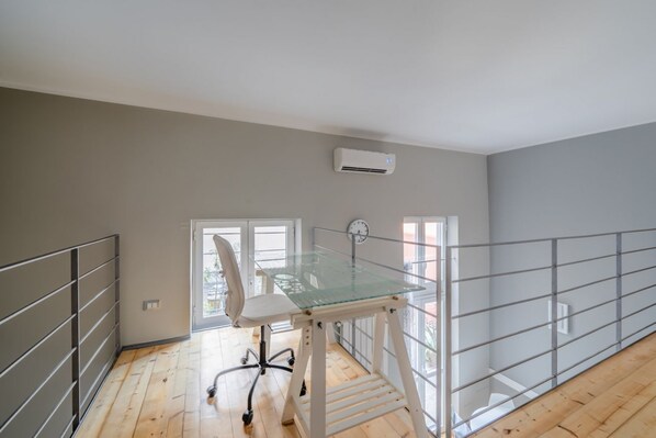 Una habitación con un escritorio de vidrio, una silla, un aire acondicionado blanco y vistas por la ventana.
