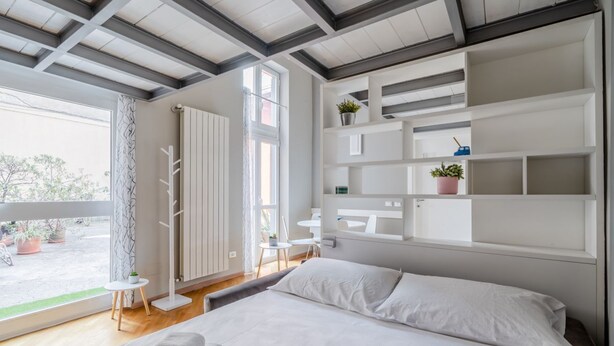 A modern bedroom with a large bed, built-in shelving, a view to the outside, and a small table by the window.