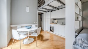 A modern kitchen with white cabinets, a dining area with a round table and white chairs, and a staircase leading to an upper level.