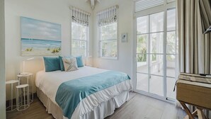 Une chambre avec un grand lit, un tableau représentant une plage et une porte-fenêtre coulissante donnant sur un balcon.