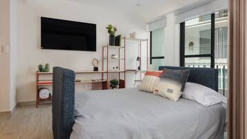 Un dormitorio moderno con una cama grande, un escritorio y una televisión, y vistas al balcón.
