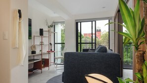 A modern living room with a grey sofa, a dining table, and a large window offering a view of the outdoors. - Choapan 28 - Lux Apartments in Condesa (Mexico City)