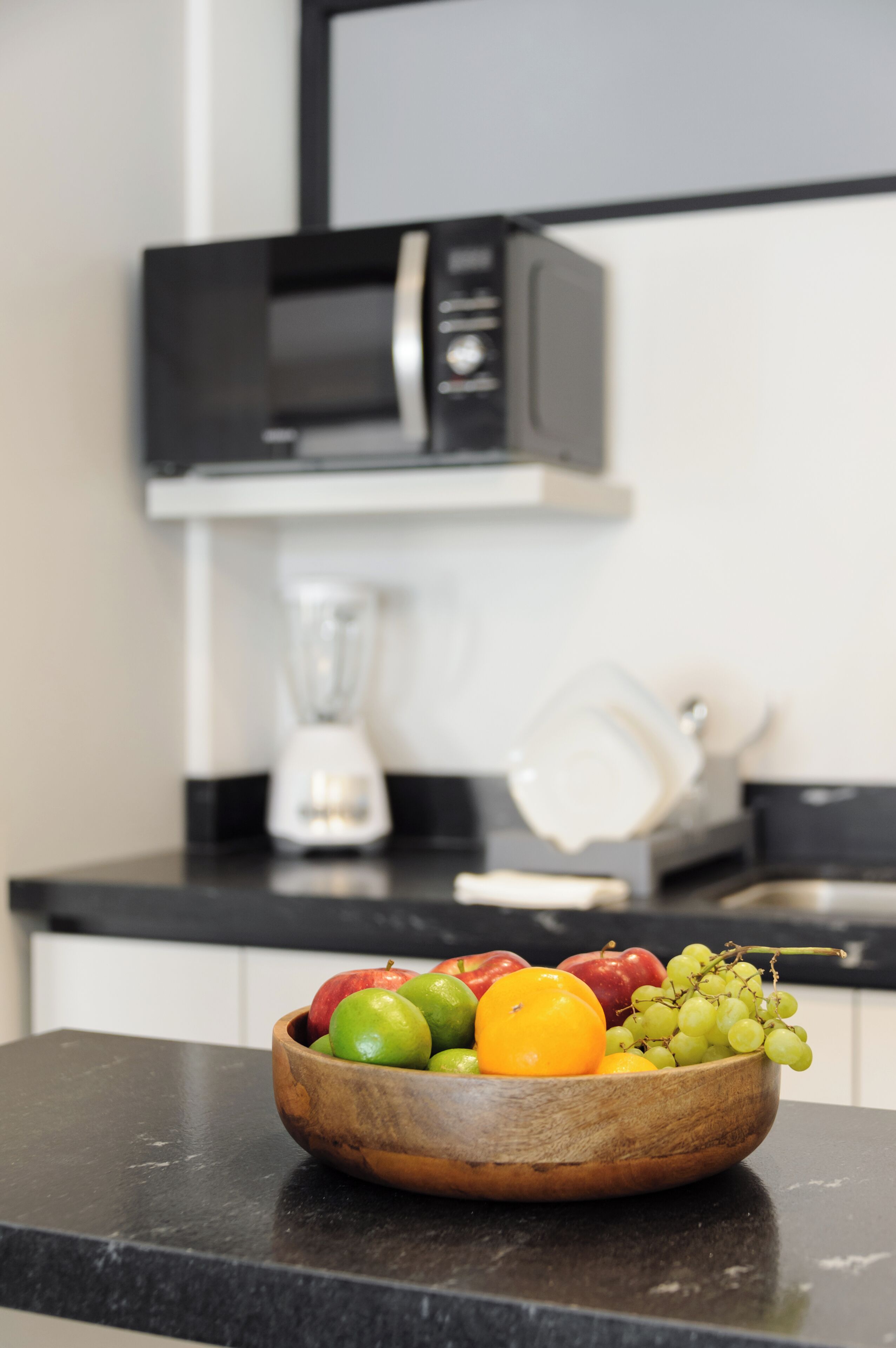 A kitchen counter with a wooden bowl of fruit and a microwave above it.