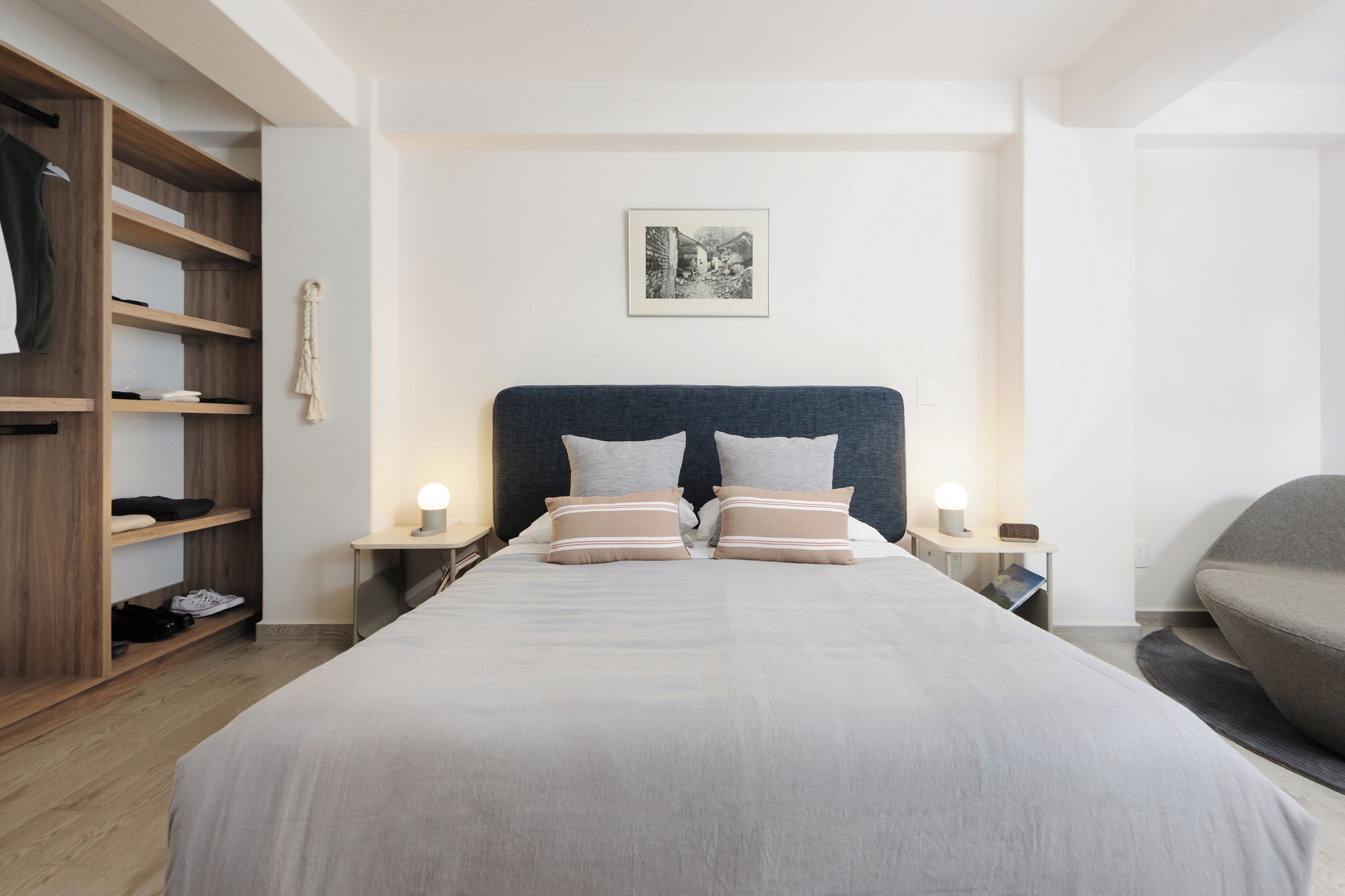 A neatly arranged bedroom with a large bed, wooden wardrobe, bedside tables with lamps, and a framed picture on the wall.
