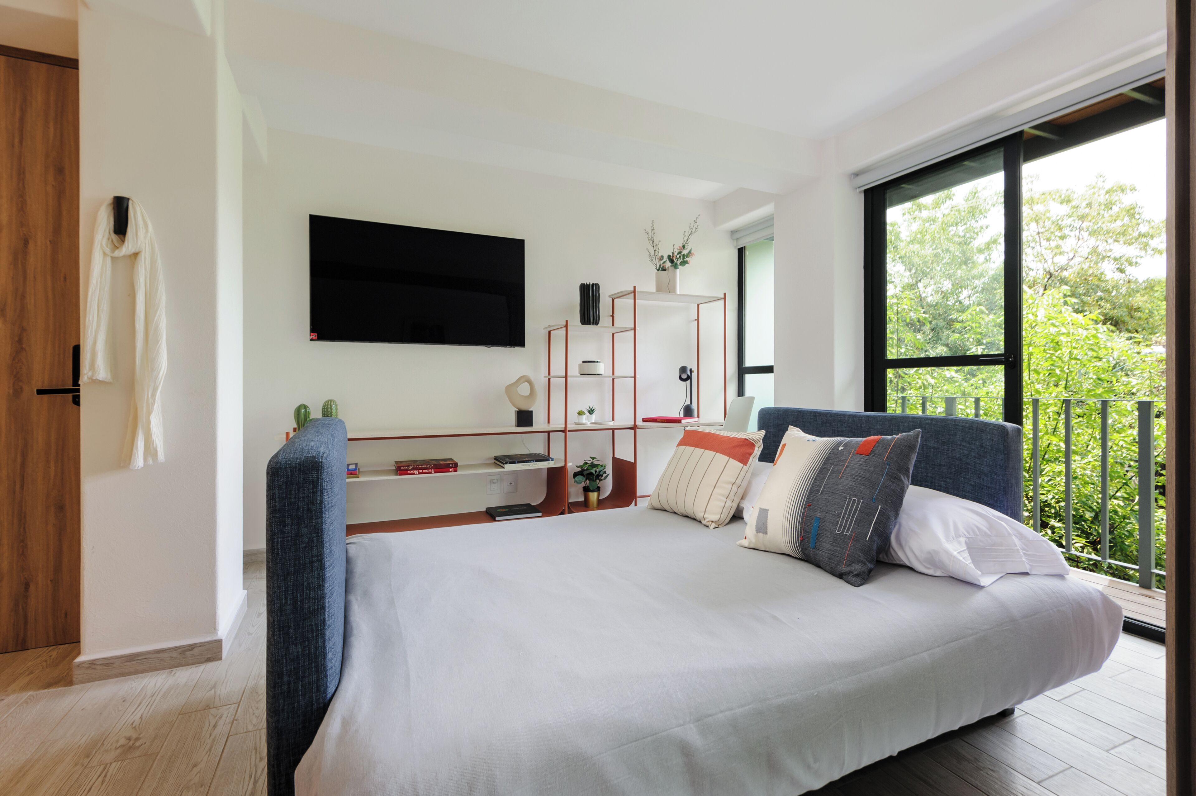 Een moderne slaapkamer met een groot bed, een aan de muur bevestigde televisie en uitzicht op groen door een groot raam.