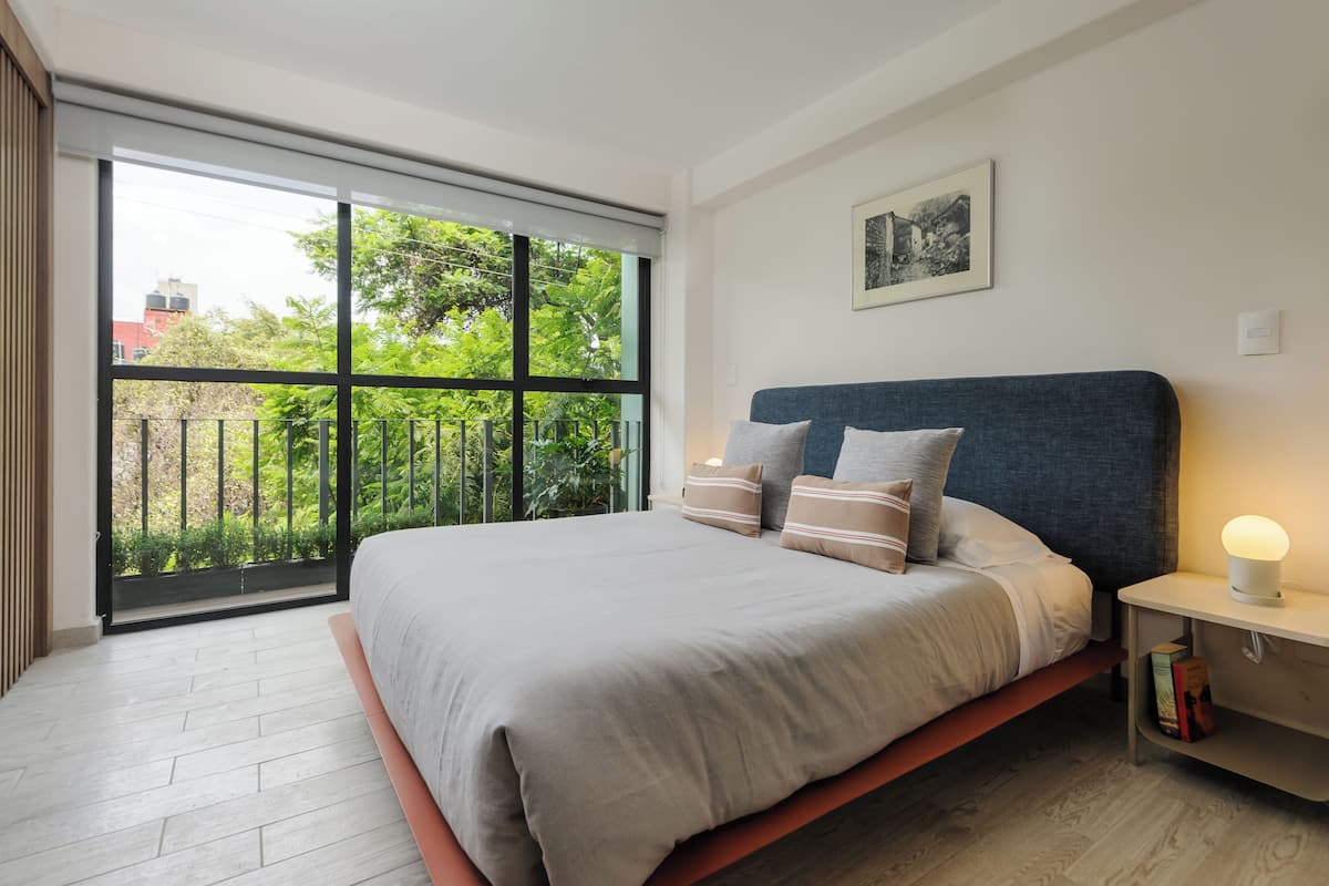 Een moderne slaapkamer met een groot bed, een nachtkastje met lamp en uitzicht op groen via een schuifdeur.
