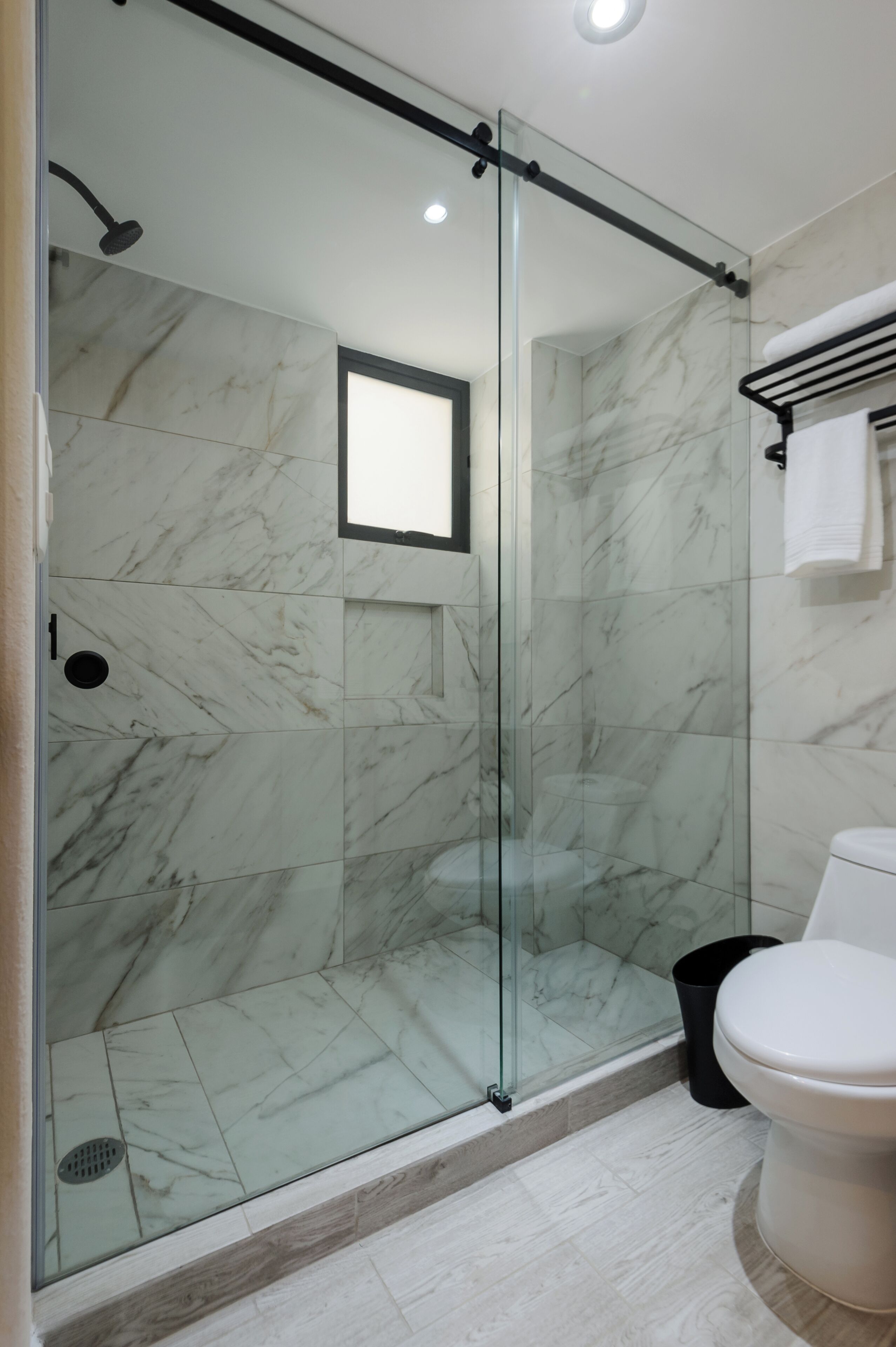 Een moderne badkamer met een douchecabine van glas, marmeren wanden en een wit toilet.