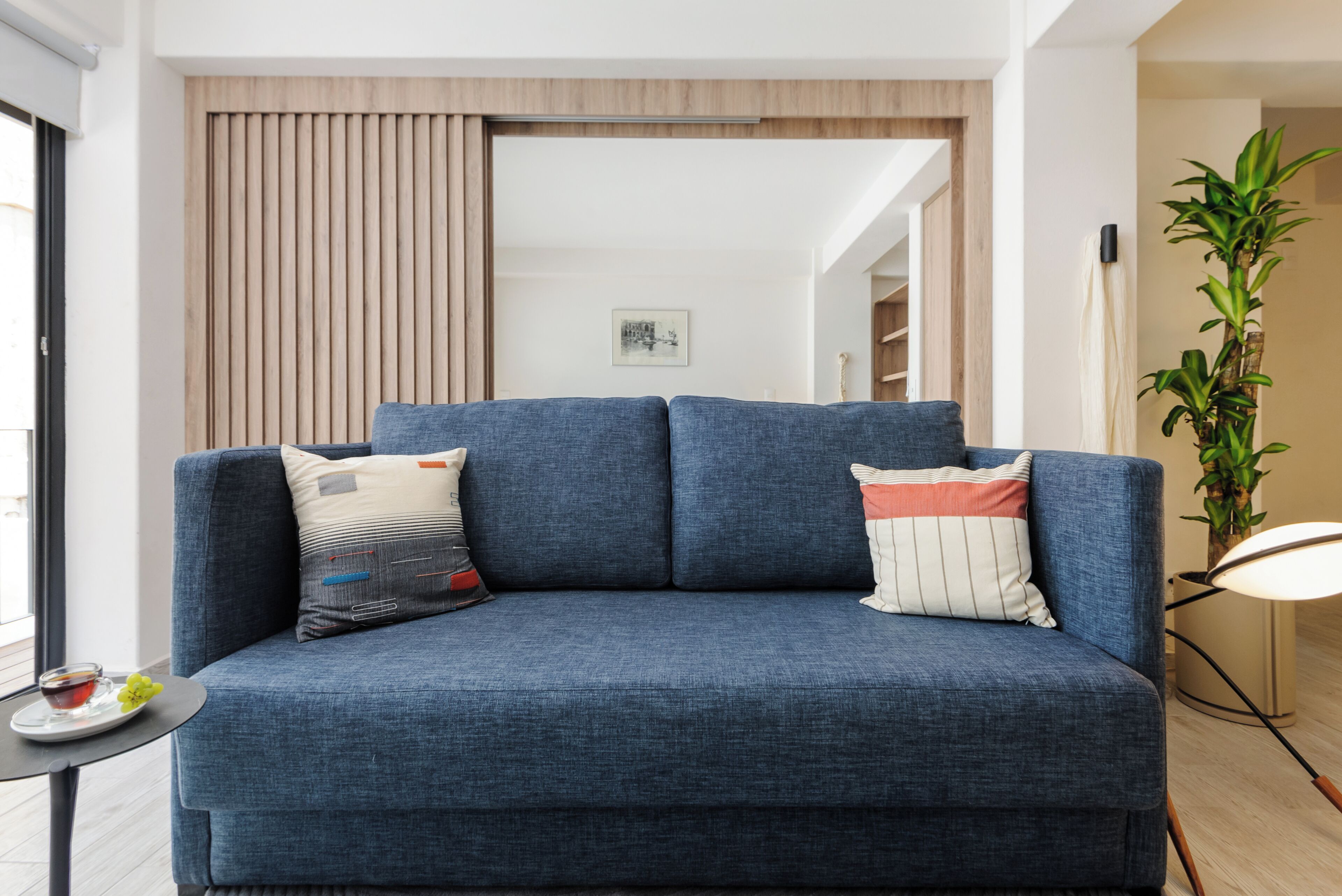 Un salon moderne avec un canapé bleu, deux coussins décoratifs, une petite table sur laquelle se trouve une boisson et une plante en pot.