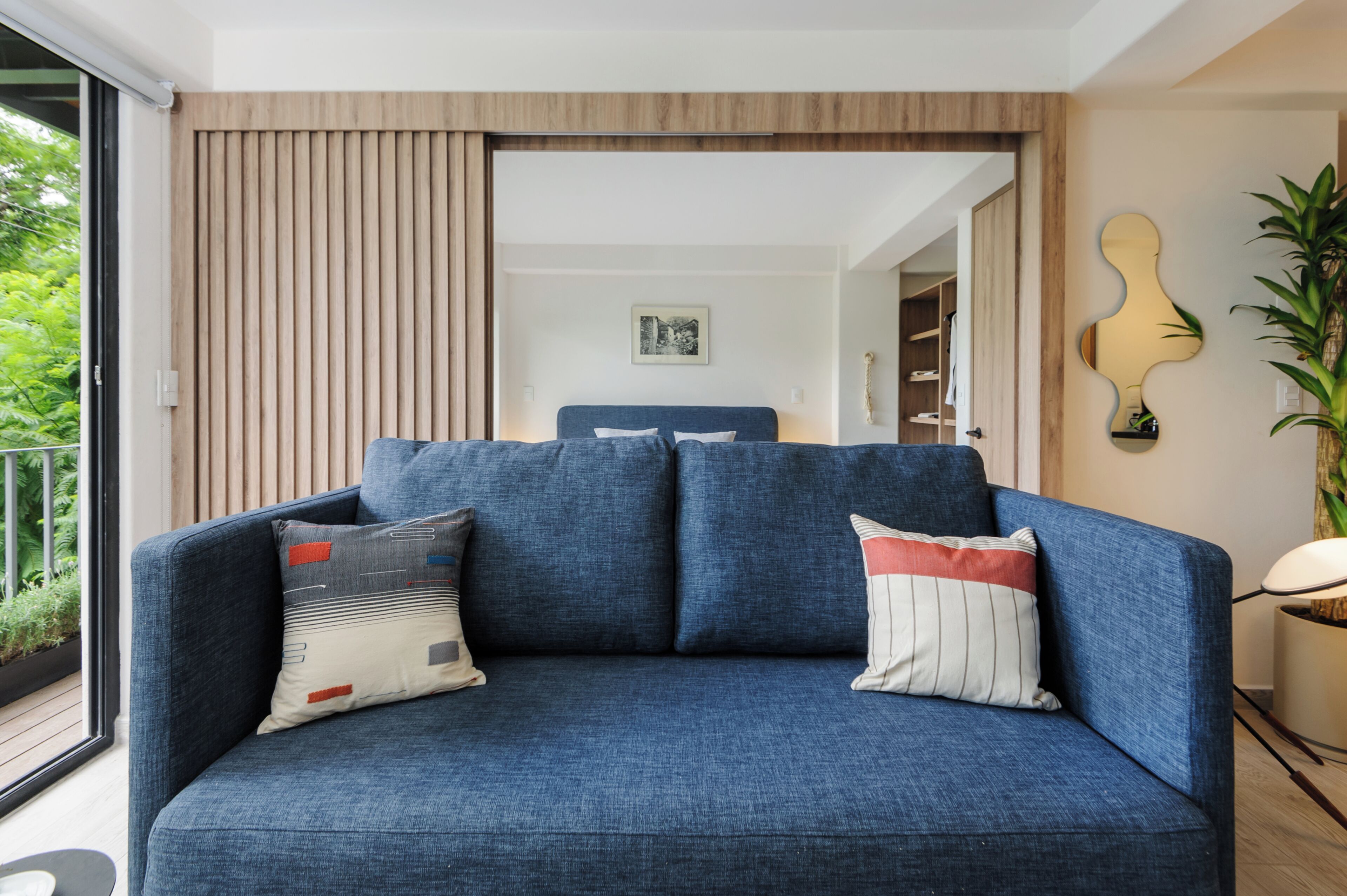 Una sala de estar moderna con un sofá azul, dos almohadas, un panel de pared de madera, un cuadro enmarcado y una planta en maceta.