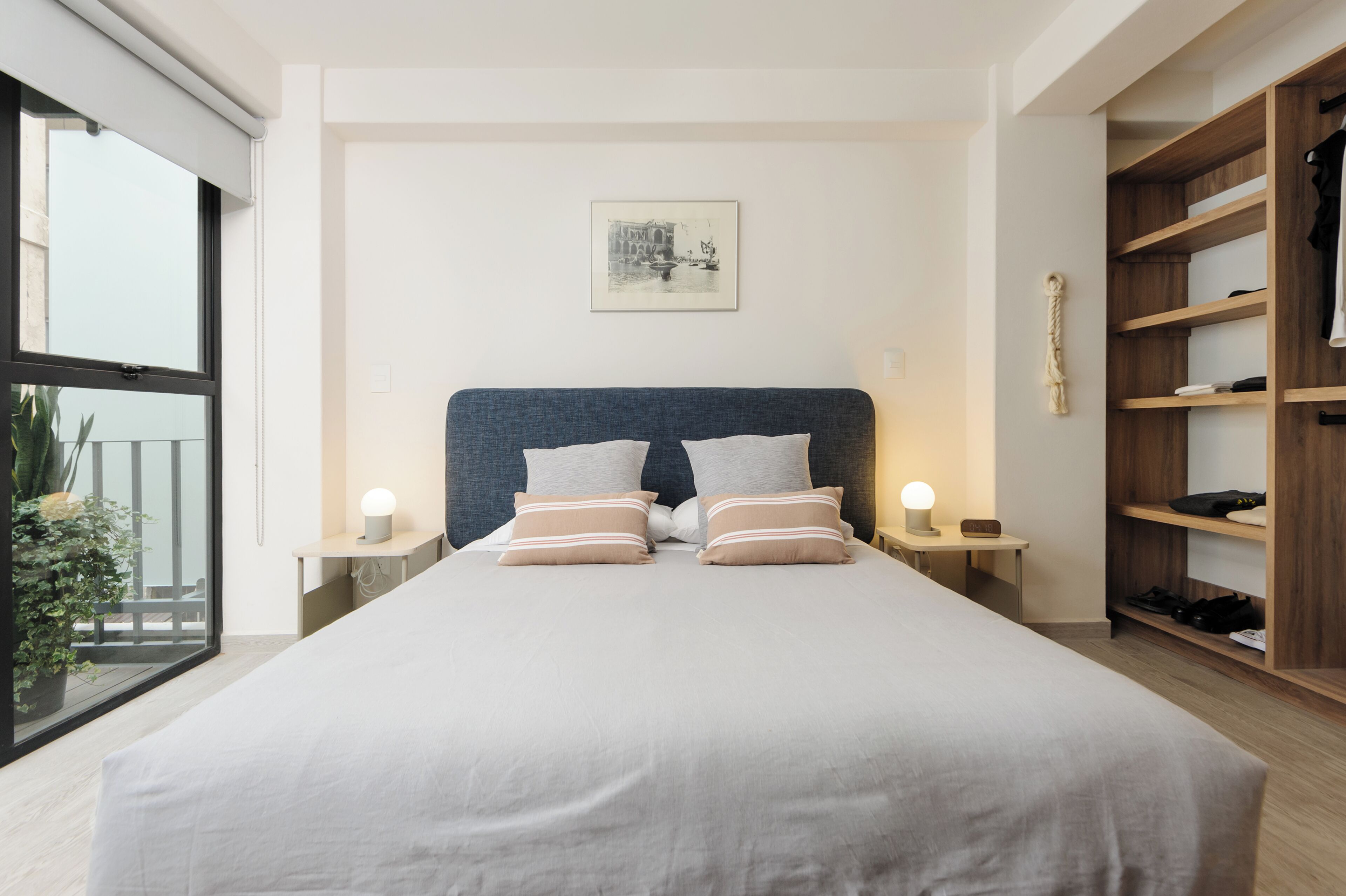Un dormitorio moderno con una cama grande, mesitas de noche, un armario de madera y vistas al balcón.