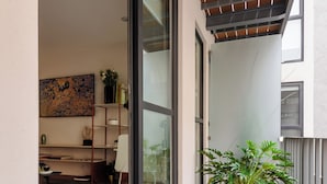 A balcony with a wooden floor, a potted plant, and a sliding glass door leading to an interior space with a desk, chair, and shelves. - Choapan 28 - Lux Apartments in Condesa (Mexico City)