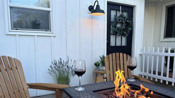 Une terrasse avec deux chaises en bois, une table, un foyer avec des flammes et une plante en pot.