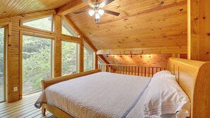 Un dormitorio de cabaña de madera con una cama, un ventilador de techo y ventanas amplias.