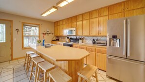 Una cocina con armarios de madera, un refrigerador de acero inoxidable, un microondas y una isla grande con taburetes de bar.