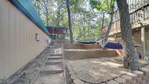 Una terraza de madera con una hamaca, un muro de ladrillo y una escalera que lleva a una zona cubierta.