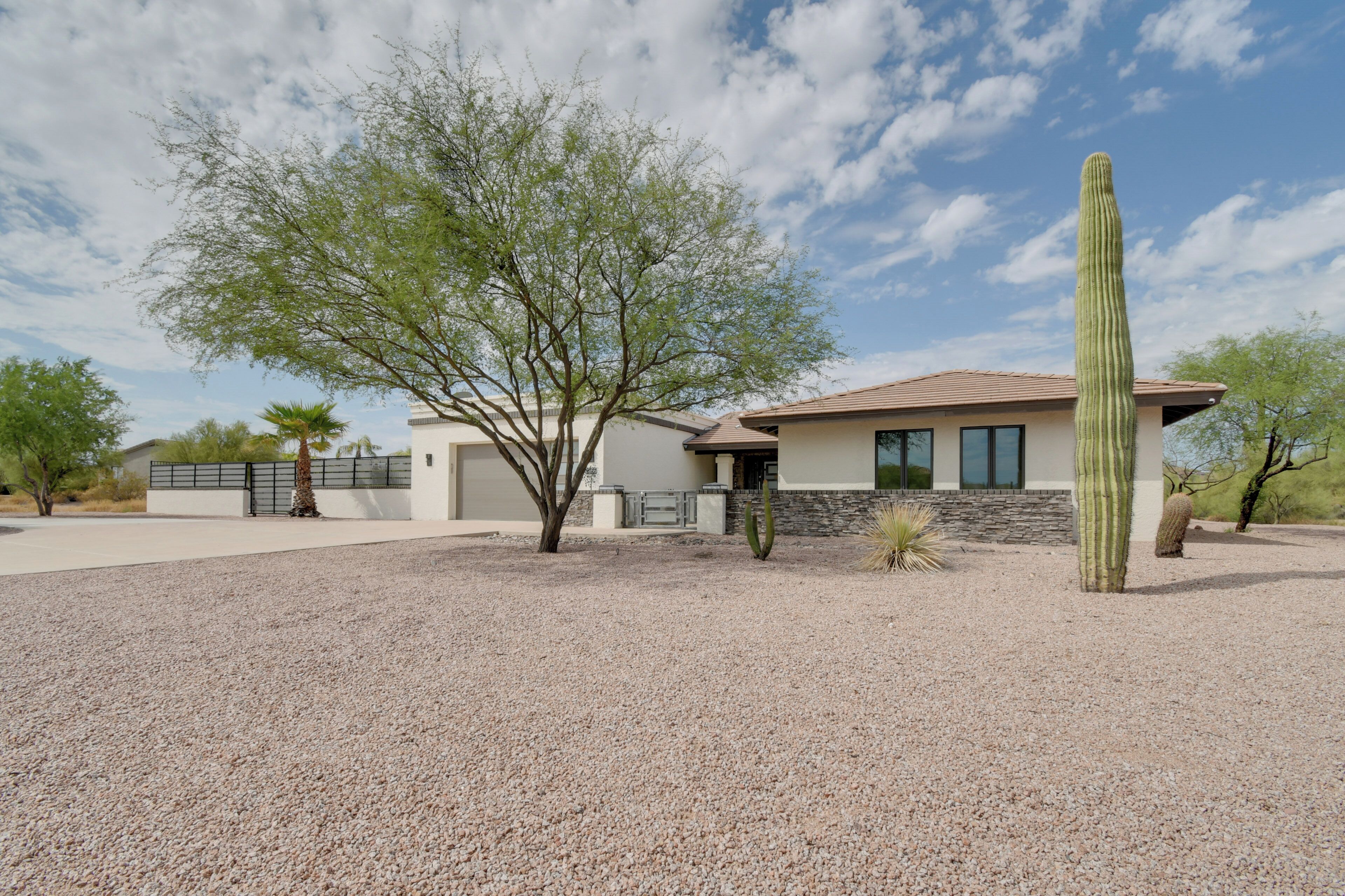 A modern house with a gravel driveway, a tall cactus, and a tree in the front yard.