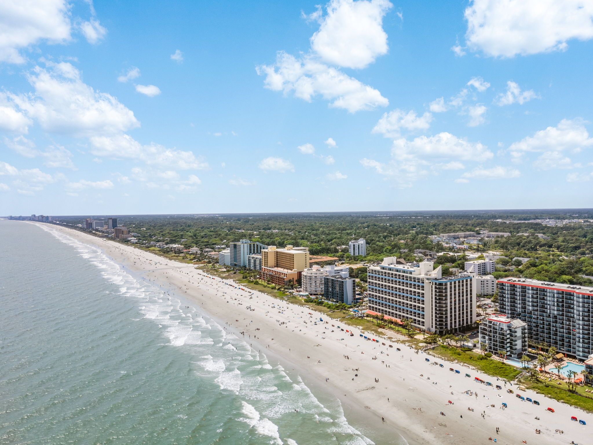 A coastal cityscape with a beach, high-rise hotels, and a clear sky.