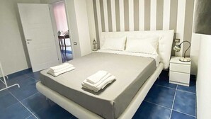 A modern bedroom with a large bed, a nightstand, and a door leading to another room. - Relais Galatea (Montecorvino Pugliano)
