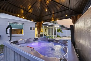 Un bain à remous sous une pergola en bois, avec une maison en arrière-plan.