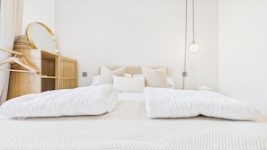 Une chambre à coucher au style minimaliste, comprenant un lit, des oreillers, une table de chevet, une lampe suspendue et une armoire en bois.