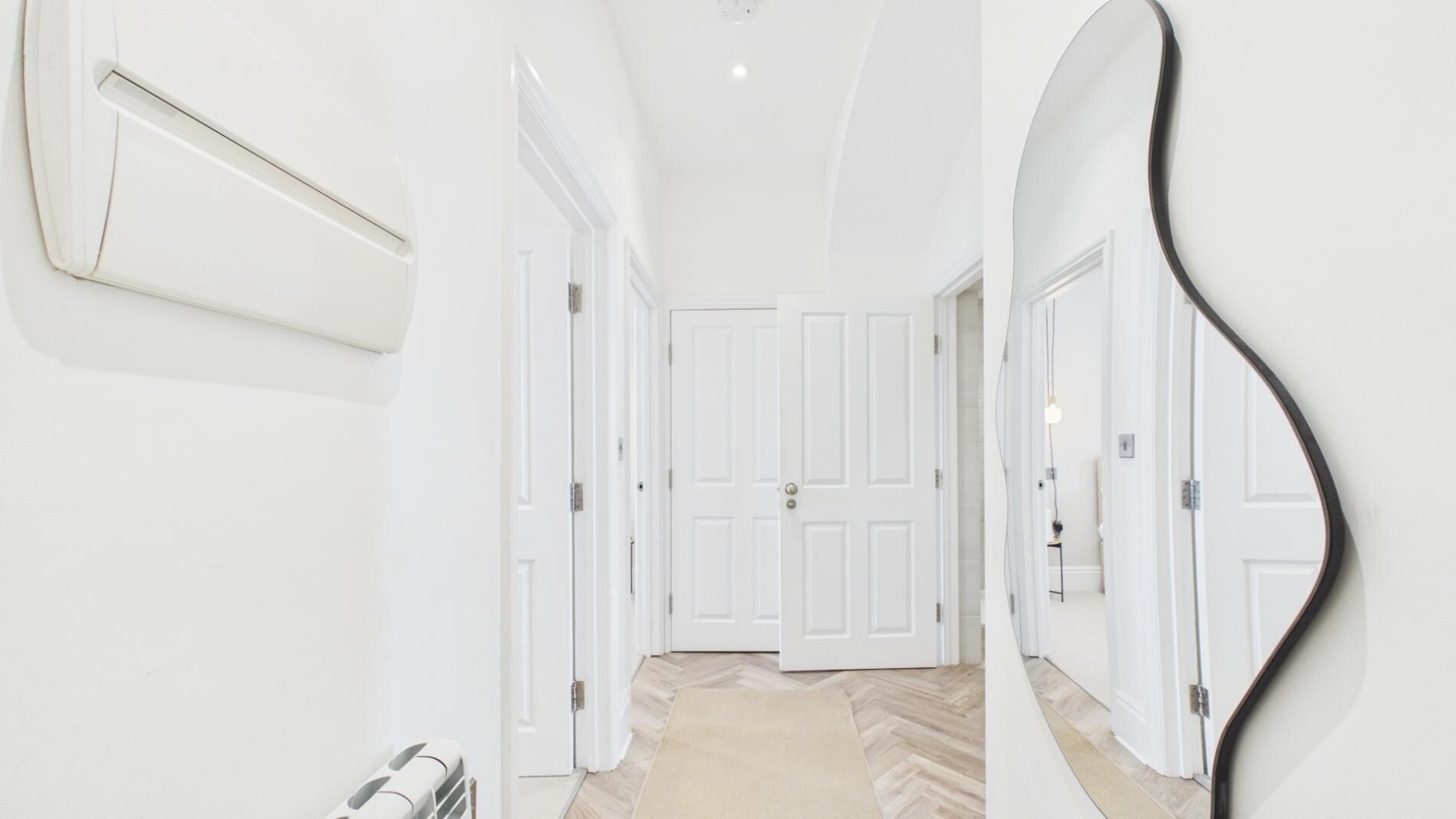 A hallway with white doors, a radiator, and a herringbone-patterned floor.