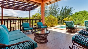 A covered outdoor seating area with wicker furniture and a glass table, overlooking a swimming pool and lush greenery. - Modern Home with Private Plunge Pool in Placencia (Placencia)