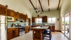 A spacious kitchen with wooden cabinets, stainless steel appliances, and a large island with bar stools. - Modern Home with Private Plunge Pool in Placencia (Placencia)