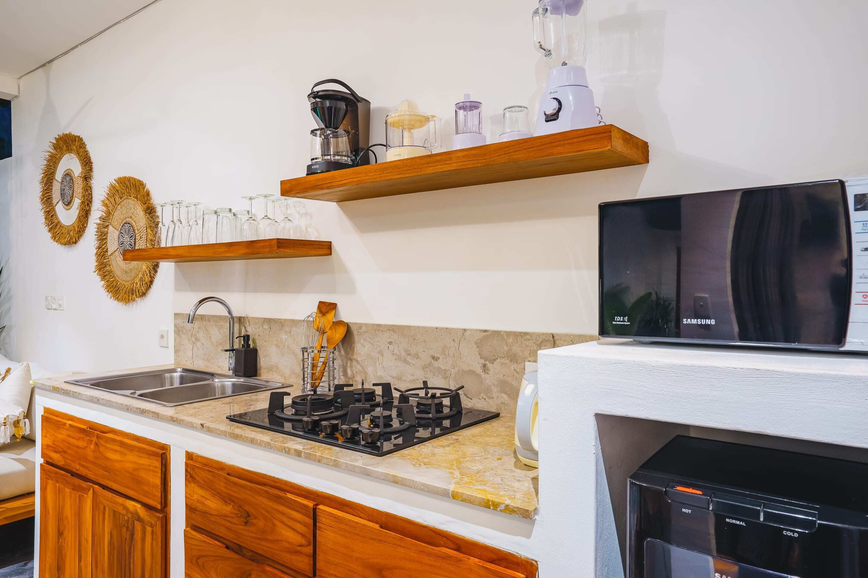 A kitchen with a gas stove, microwave, and a Samsung refrigerator. There are wooden shelves above the counter holding various kitchen items.