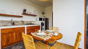 A modern kitchen with wooden cabinets, a dining table set for four, and a hanging light fixture. - Villa Karina (Tabanan)