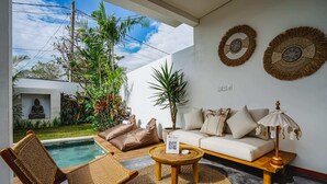 A modern living room with a pool, a sofa, and a chair. There are decorative wall hangings and a small table with a lamp. - Villa Karina (Tabanan)