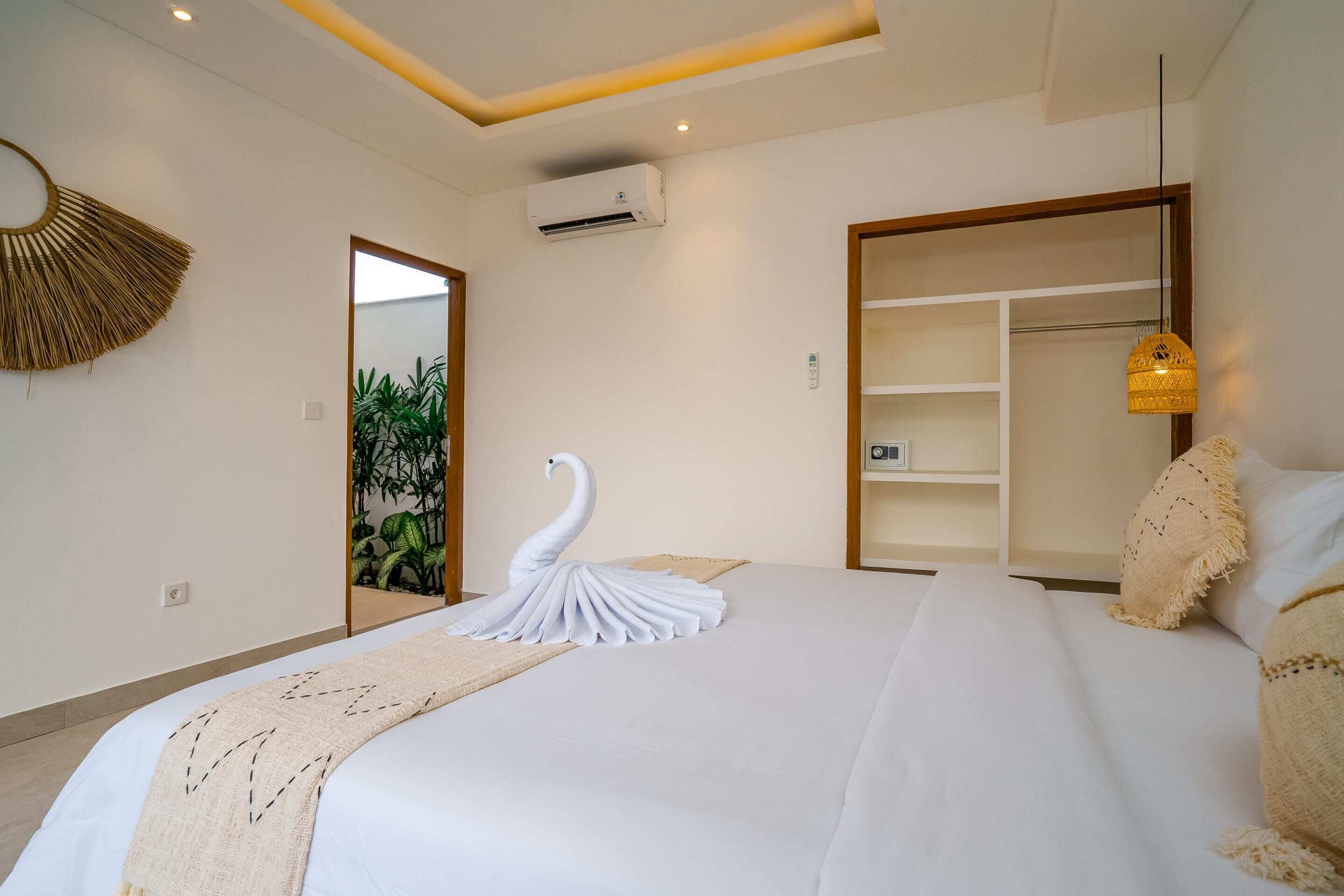 A hotel room with a large bed, a mirror, an air conditioning unit, a wardrobe, and a hanging light fixture.