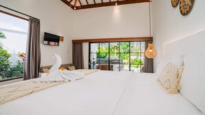 A hotel room with a large bed, a TV mounted on the wall, and a view of greenery outside. - Villa L at Seseh (Munggu)