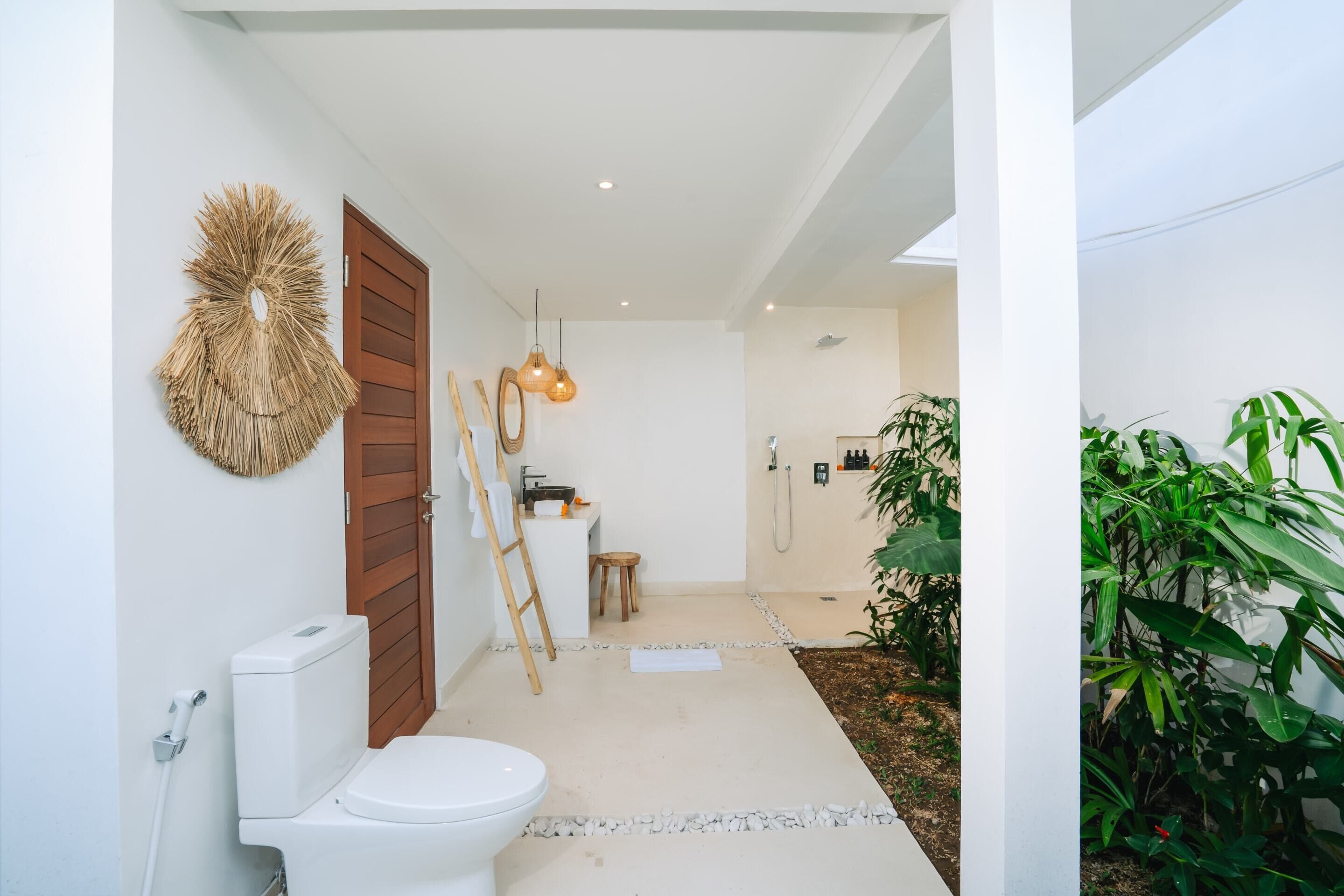 A modern bathroom with a toilet, sink, and shower area. There are wooden doors, a ladder, and a hanging light fixture.