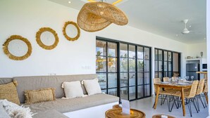 A modern living room with a grey sofa, wooden side tables, and a dining area with a wooden table and chairs. - Villa L at Seseh (Munggu)