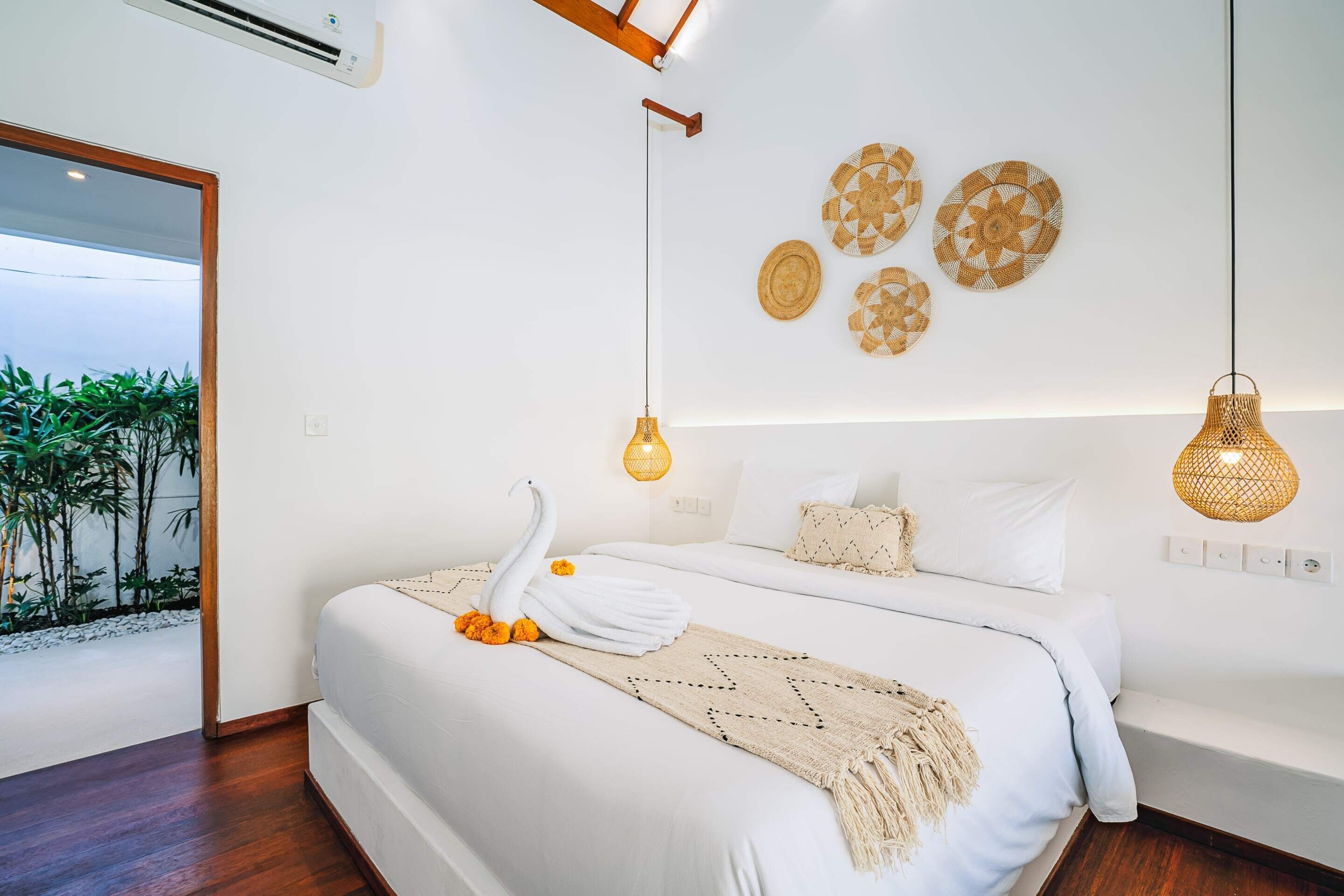 A modern bedroom with a large bed, decorative wall art, and a view of greenery outside.