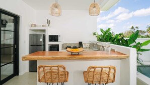 A modern kitchen with a wooden island, wicker chairs, and hanging pendant lights. - Villa L at Seseh (Munggu)