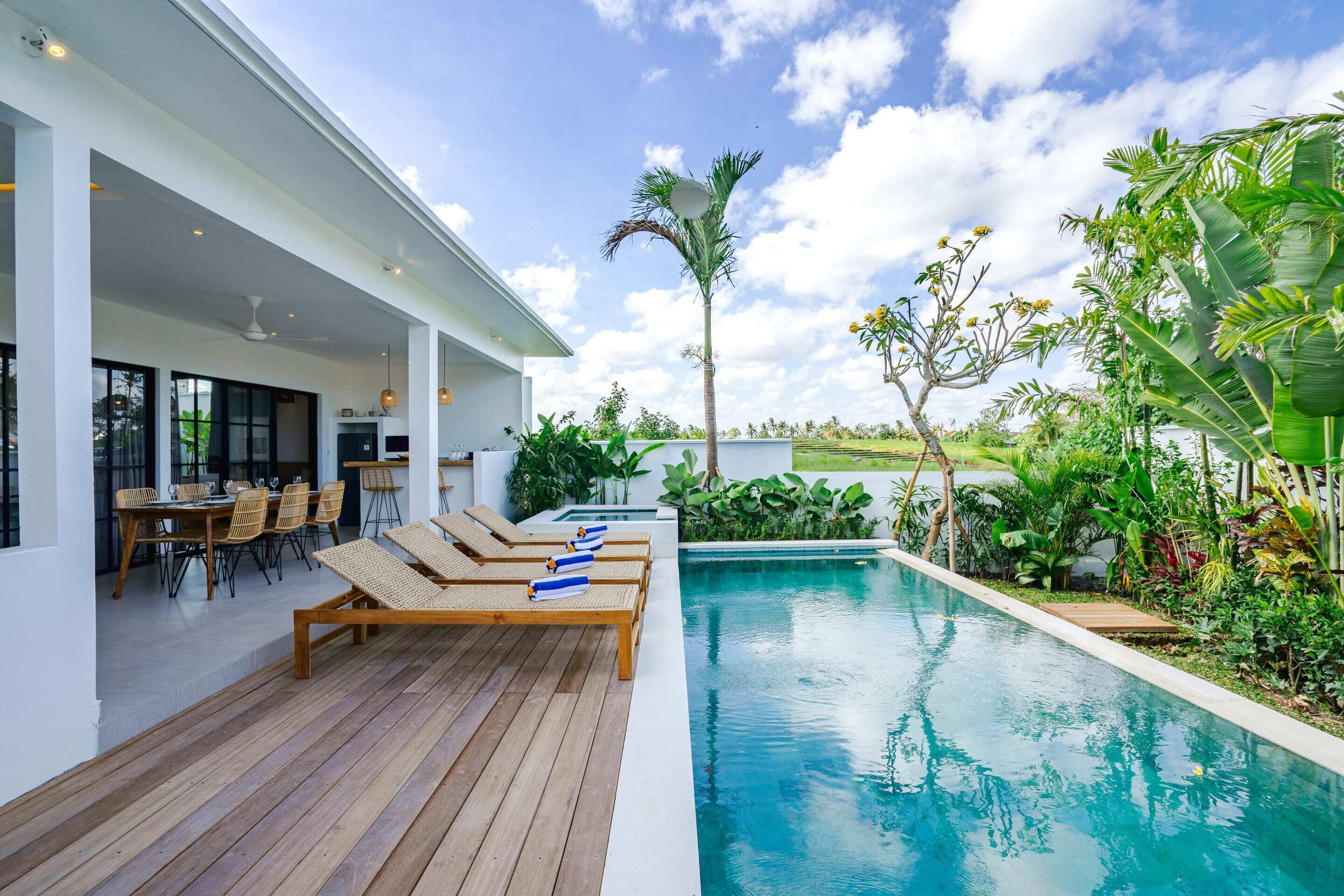 A modern outdoor pool area with lounge chairs, a dining area, and lush greenery.