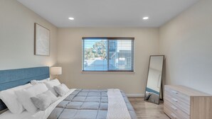 Ein Schlafzimmer mit Bett, Nachttisch, Lampe, Kommode und einem Fenster mit Jalousien.