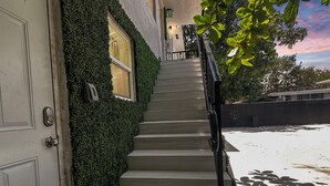 Una escala porta a una porta amb un tancat de codi, tot voltat per un arbustos.