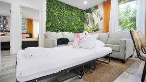 Una habitació d'hotel moderna amb llit, sofà, paret verda i finestra amb cortines.